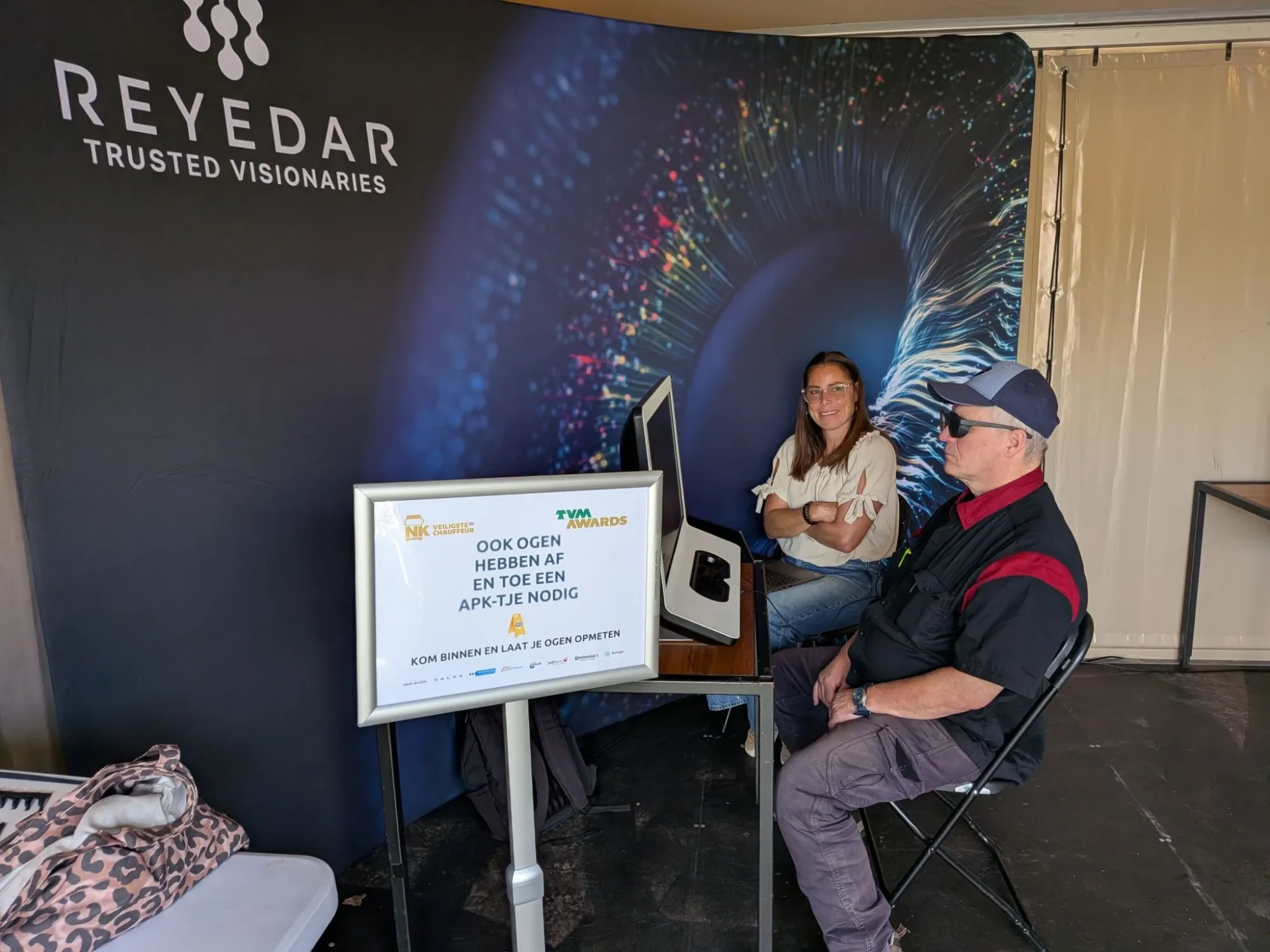 A professional driver taking the vision check at the Reyedar stand, beside a sign inviting drivers to have their eyes measured